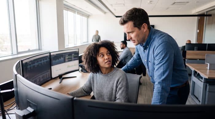 Two colleagues reviewing data on a bank of monitors in an operations room